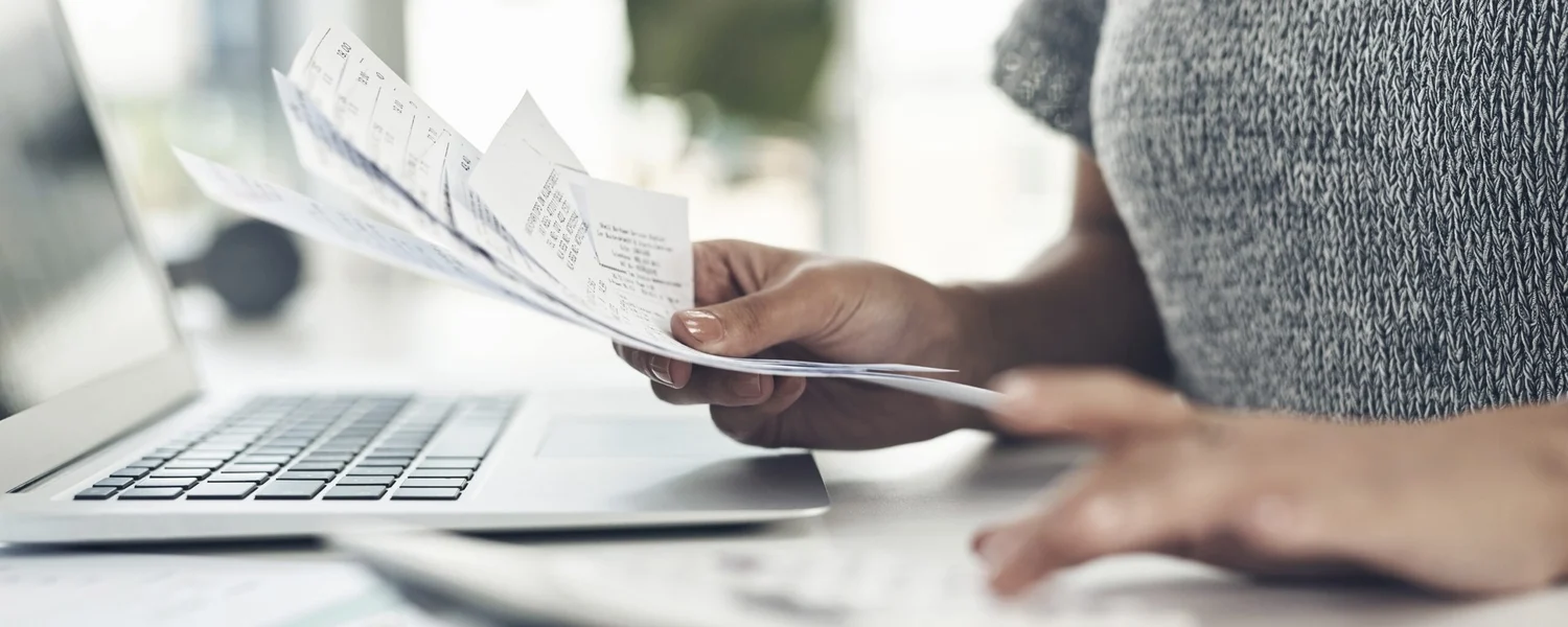 A woman's hand sorting through paper receipts in front of a laptop