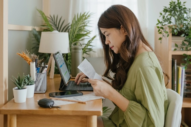 A woman working on a tablet computer while holding a piece of paper